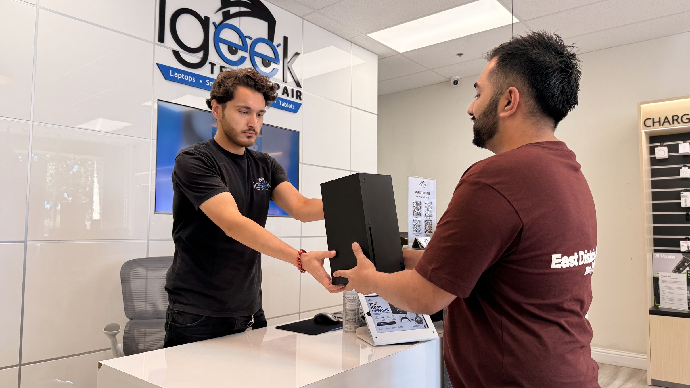 iGeek technician handing a repaired game console back to a customer at the Elk Grove counter